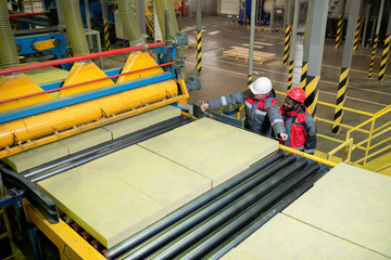 Horizontal high angle shot of two professional factory workers measuring heat-insulating slab size