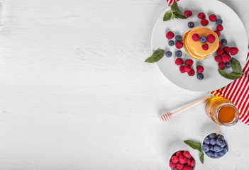 Tasty american pancakes with raspberries, blueberries and honey on white wood background. Top view. Copy space.