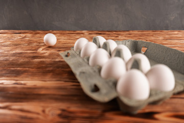 A lone egg is thrown near a package of eggs on a wooden table.