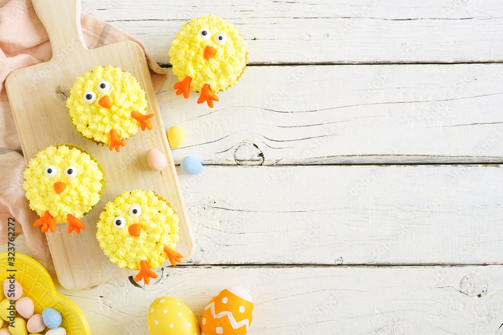 Poster spring chick cupcakes. top view table scene. side border with copy space against a white wood backgr