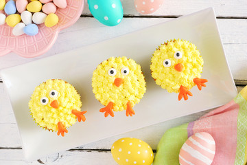 Cute Easter chick cupcakes. Top view table scene with a white wood background.