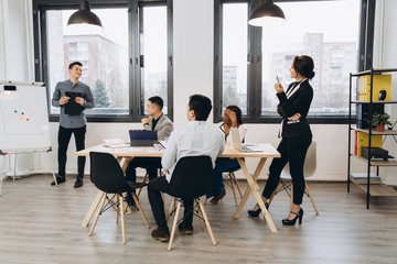 Group of positive multicultural marketing experts planning working process and sharing ideas while creating advertising campaign.Young colleagues collaborating together in loft interior office