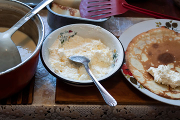 Cooking pancakes with cottage cheese at home. Pancake lies on a plate. Nearby there is cottage cheese, a red spatula for removing pancakes and a pan with dough.