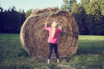Naklejka na ściany i meble Child girl playing on a bale of straw on a field