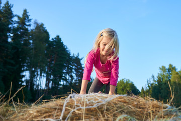 Naklejka na ściany i meble Child girl playing on a bale of straw on a field