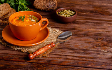 Vegetarian autumn cream soup of pumpkins and carrots with seeds and parsley on a wooden background with copy space, flat lay