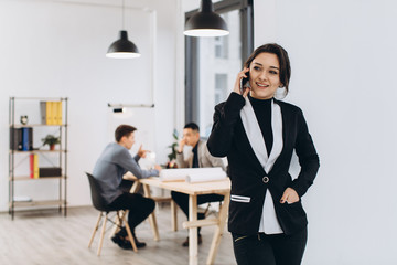 Business woman with mobile phone, people group in background at modern bright office indoors