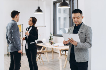 Asian business man with his tablet, people group in background at modern bright office indoors