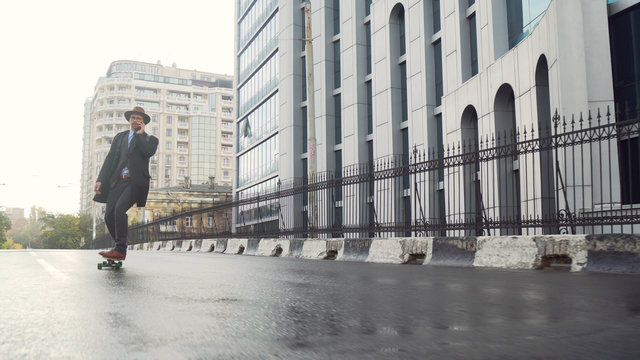Businessman skateboarding near office center and using cell phone by business