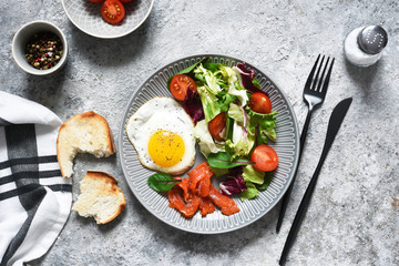 Classic breakfast - fried eggs with salad and salmon with fried toast on the kitchen table.