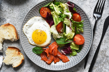Classic breakfast - fried eggs with salad and salmon with fried toast on the kitchen table.