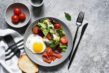 Classic breakfast - fried eggs with salad and salmon with fried toast on the kitchen table.
