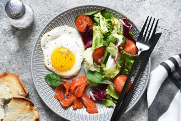 Classic breakfast - fried eggs with salad and salmon with fried toast on the kitchen table.