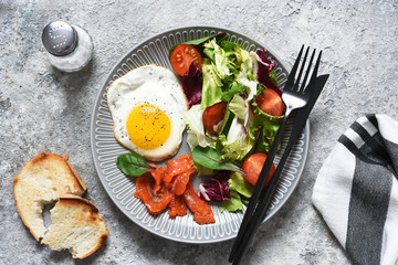 Classic breakfast - fried eggs with salad and salmon with fried toast on the kitchen table.