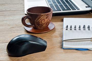 Cup of coffee, laptop and notebook with pen on wooden table