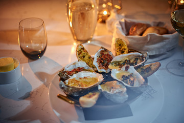 Haute cuisine and luxury dinner golden metallic bowl of prepared oysters and crispy bread loafs with sauce and vegetable spread served on a white stone table next to candle, a glass of white wine