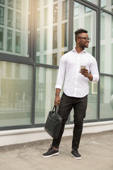 handsome young african man in a white shirt with a phone in his hands near a glass building