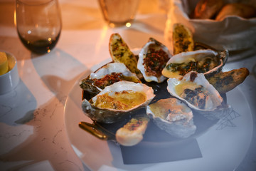 Rich and luxury dinner golden metallic bowl of prepared oysters and crispy bread loafs with sauce and vegetable spread served on a white stone table next to candle, jellyfish in a glass stone