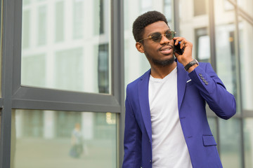 handsome young african man in a suit with a phone in his hands near a glass building