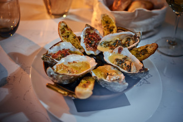 Rich and luxury dinner golden metallic bowl of prepared oysters and crispy bread loafs with sauce and vegetable spread served on a white stone table next to candle, a glass of white wine, jellyfish in