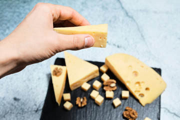 .In hand a piece of cheese with walnuts on a dark background.
