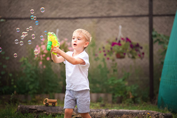 Soap Bubble Games. The boy in the backyard is playing with a water gun. Boy in summer playing with...