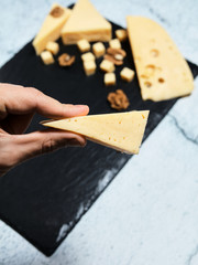 .In hand a piece of cheese with walnuts on a dark background.
