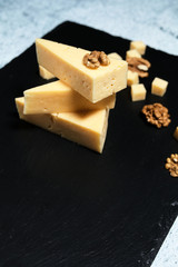 Pieces of cheese with walnuts on a dark background.