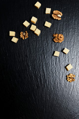 Pieces of cheese with walnuts on a dark background.