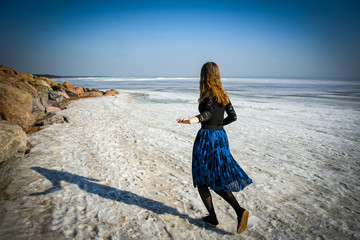 Girl walks on snow covered shore of frozen sea - Powered by Adobe