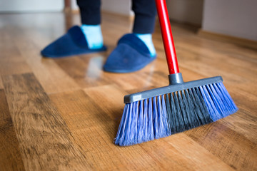 Wife in blue slippers using indoor blue broom for hardwood floor cleaning.