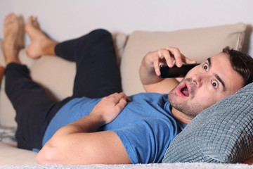 Shocked man calling by phone from the sofa 