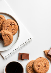 Cookies, chocolate, notepad and paper cup of coffee on a white background, top view, flat lay, free space for text. Sweet breakfast, copy space.