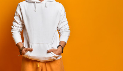 man in a white sweatshirt, pants and bracelets. Folded hands in pockets and posing on an orange...