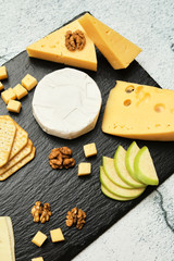 Pieces of cheese on a dark background. Cheeseboard. Sliced ​​apple and nuts on the board. Hard cheese, camembert, roquefort, emmental.