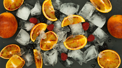 Zenithal view of Blood Oranges and berries on crushed ice on a black slate background. Healthy food concept.