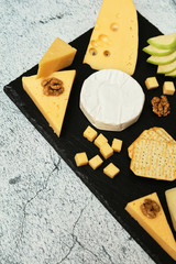 Pieces of cheese on a dark background. Cheeseboard. Sliced ​​apple and nuts on the board. Hard cheese, camembert, roquefort, emmental.