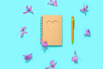 Notepad with pen and dried orchids buds on blue background. Eco friendly materials concept.