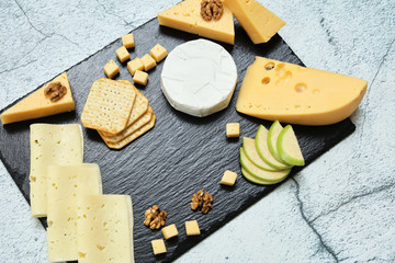 Pieces of cheese on a dark background. Cheeseboard. Sliced ​​apple and nuts on the board. Hard cheese, camembert, roquefort, emmental.