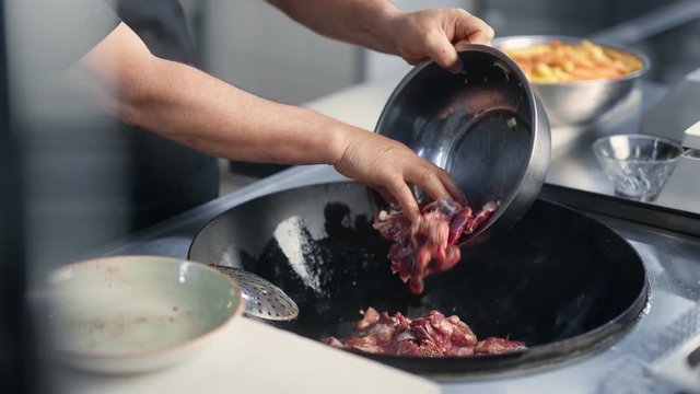 Male chef hands adding raw meat to frying pan cooking at restaurant. Close up shot on 4k RED camera