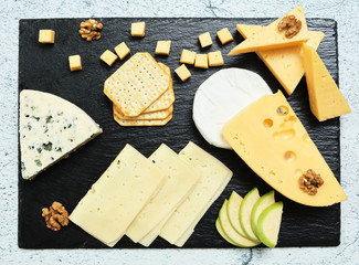 Pieces of cheese on a dark background. Cheeseboard. Sliced ​​apple and nuts on the board. Hard cheese, camembert, roquefort, emmental.