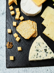 Pieces of cheese on a dark background. Cheeseboard. Sliced ​​apple and nuts on the board. Hard cheese, camembert, roquefort, emmental.