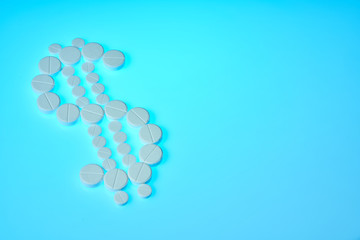 Dollar sign made from white pills on a blue background. Pharmaceutical business. Pharmacy business, medicine pill concept.