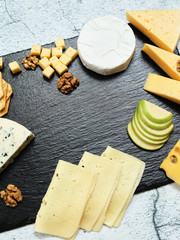 Pieces of cheese on a dark background. Cheeseboard. Sliced ​​apple and nuts on the board. Hard cheese, camembert, roquefort, emmental.