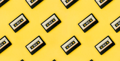 Seamless pattern with audio cassettes flat lay on colorful yellow background top view. Creative fashion design in minimal retro 80-s style. Music, radio, dj concept. Web banner template. Stock photo.