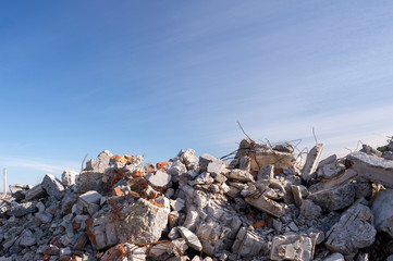 A pile of large gray concrete fragments with protruding fittings against a blue cloudy sky....