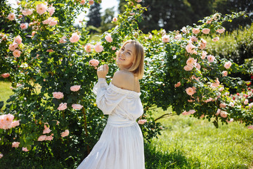 Obraz na płótnie Canvas girl in a white dress in the garden of tender pink roses