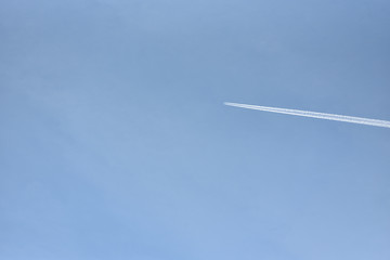 A passenger plane flies high in the sky and leaves a white trail against the blue sky. Text space