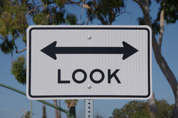 Close-up view of a traffic sign at a railroad crossing commanding to look in both directions, left...