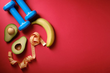 Small dumbbells, banana, avocado on a red background, a place for an inscription